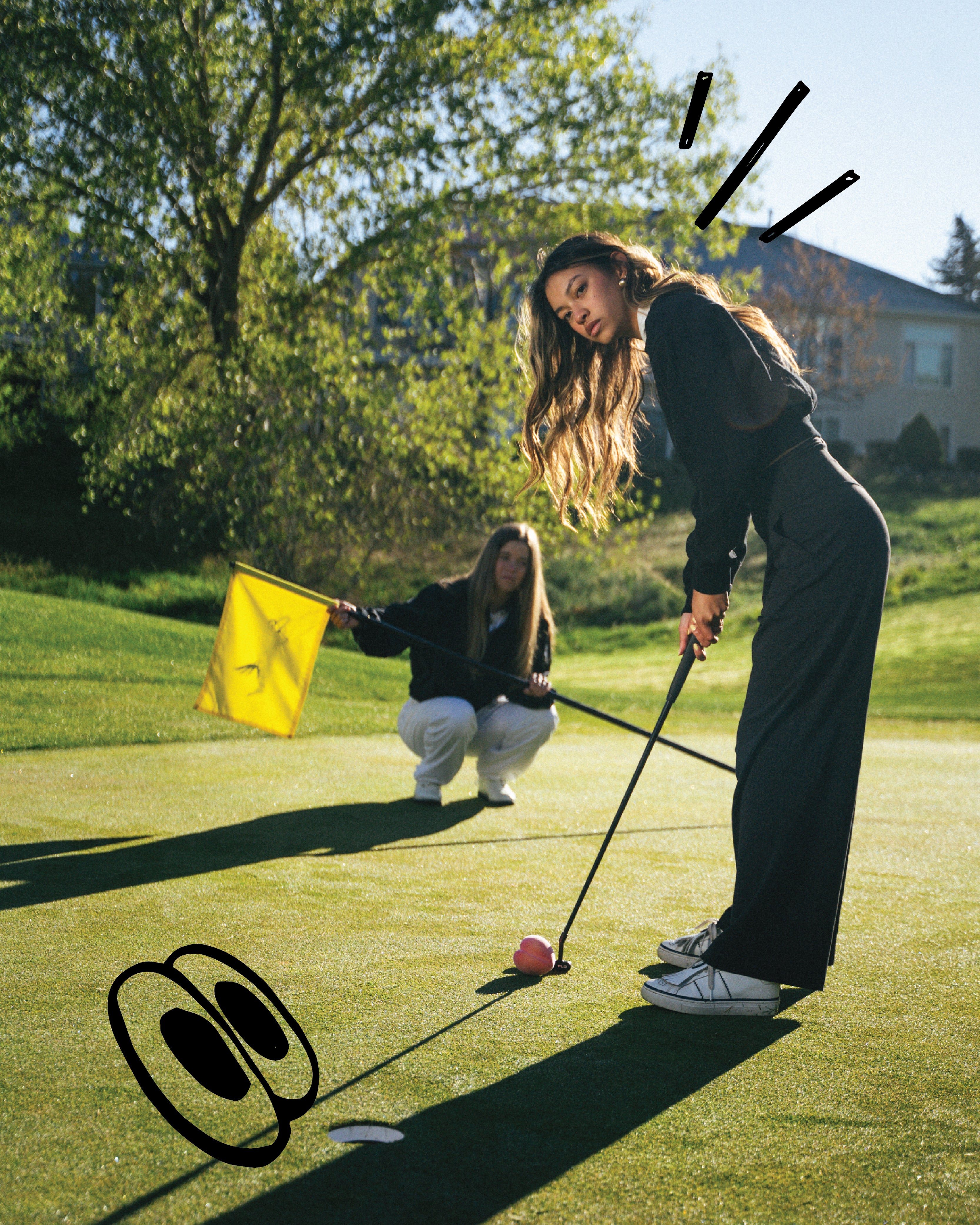 Two women play golf on a sunny green course. One woman in dark clothing putts a pink golf ball, while another holds a yellow flag in the background.
