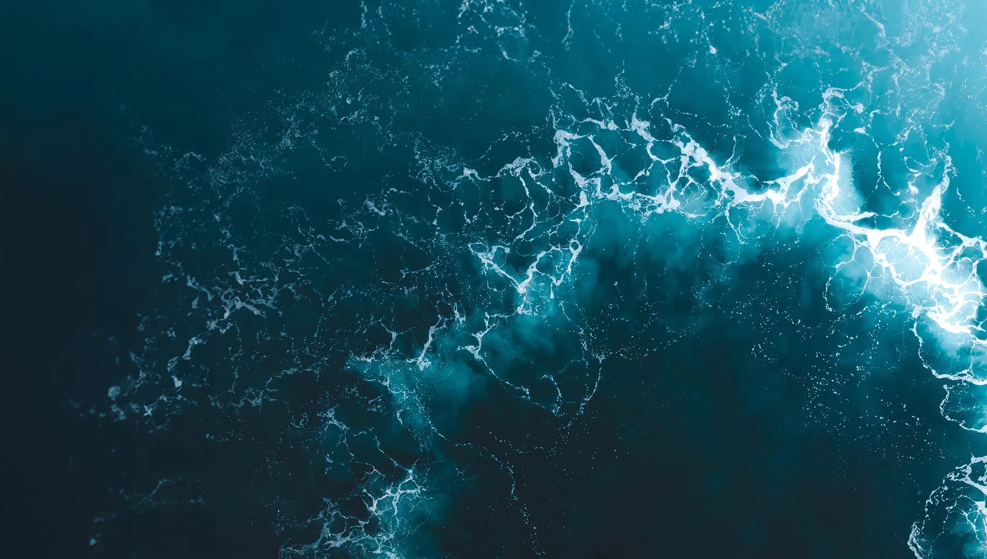 An aerial shot of the ocean with a white wave pattern.
