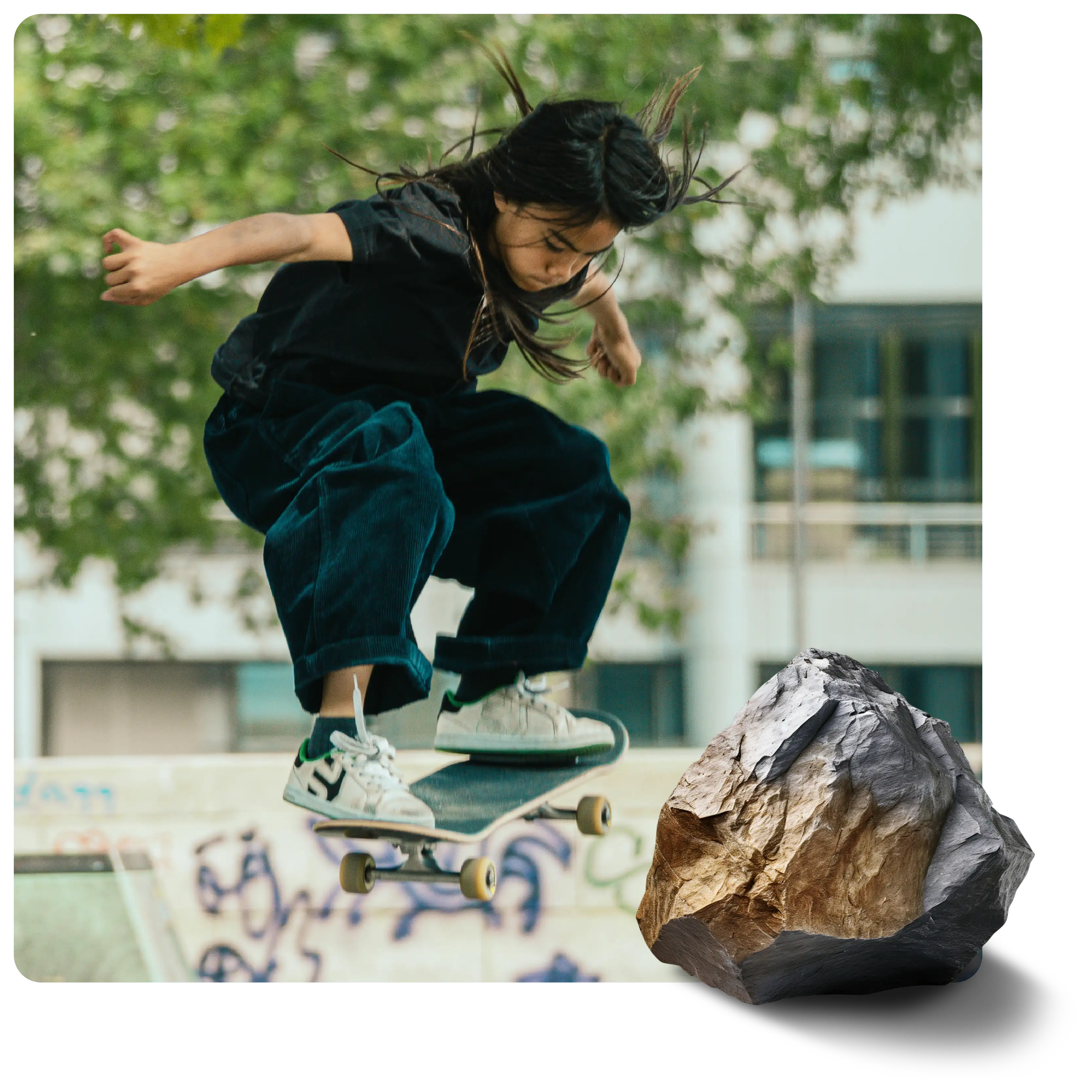 Skateboarder in black shirt, dark pants, mid-air with flowing hair over a blurry outdoor skatepark. Large brown and grey rock in foreground.