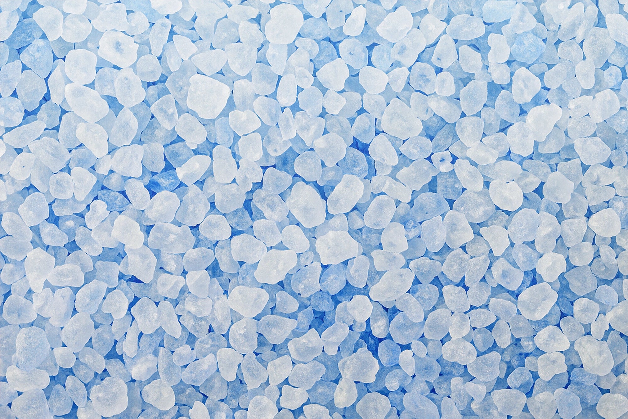 Irregularly shaped, translucent white and light blue crystals scattered across a blue surface.