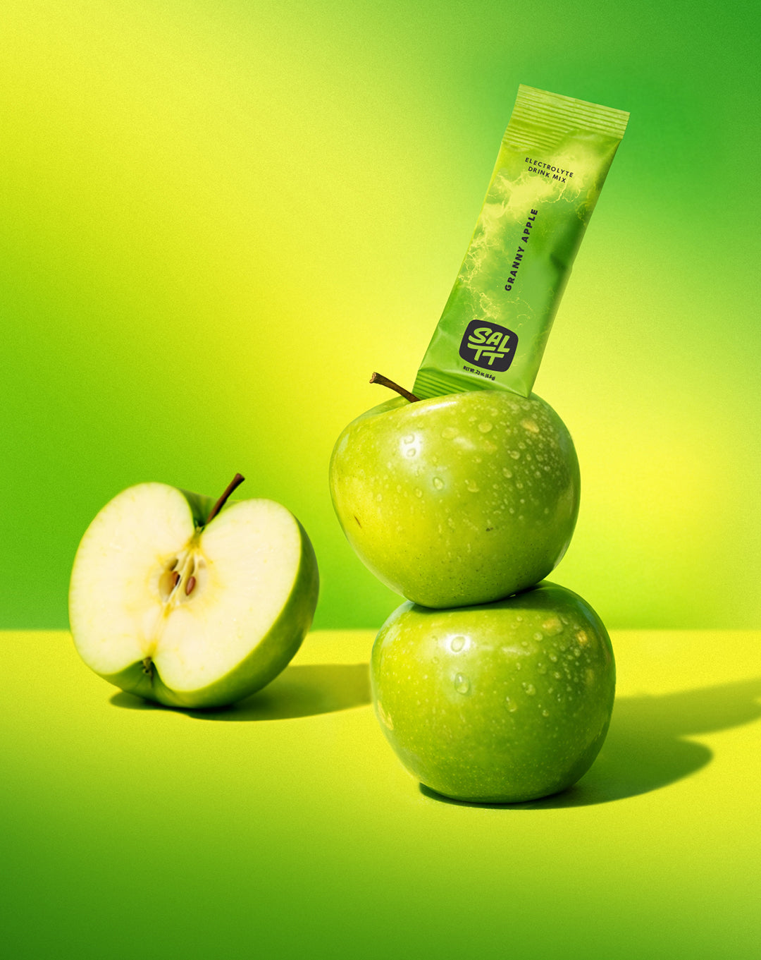 SALTT Granny Apple Electrolyte Drink Mix stick, green ocean splash. Zero sugars, dyes, citric acid. Apples on green-yellow gradient.