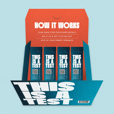 Open teal and orange 'THIS IS A TEST' box with four dark blue 'THIS IS A TEST' stick packs. White text on flap explains use.
