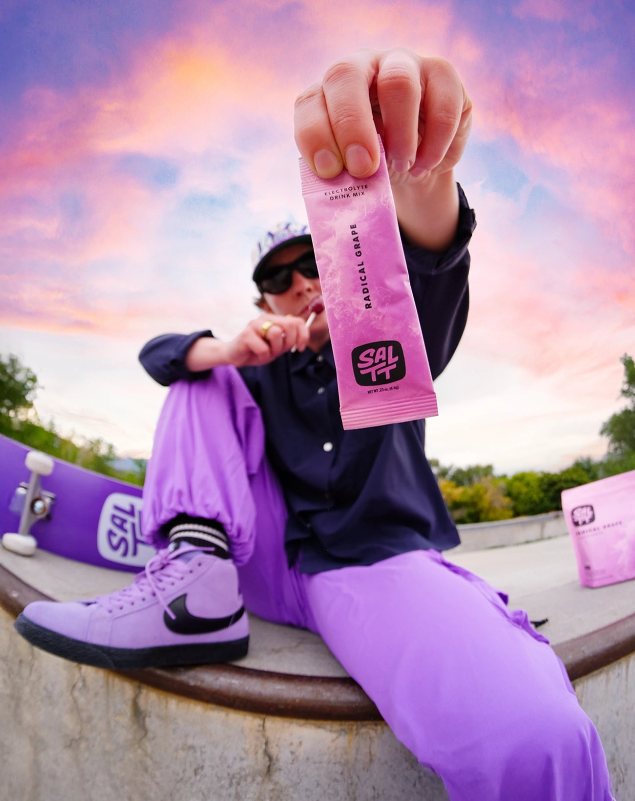 Person in purple outfit holding a SALTT Electrolyte Drink Mix Radical Grape packet to the camera.
