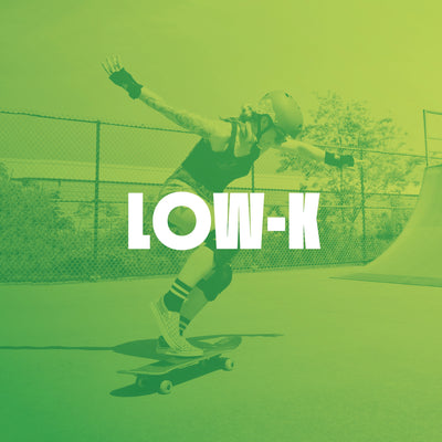 White brand name LOW-K in large text on a green-to-yellow gradient background, overlaying an image of a person skateboarding. The person wears black protective gear including wrist guards with a small graphic logo.