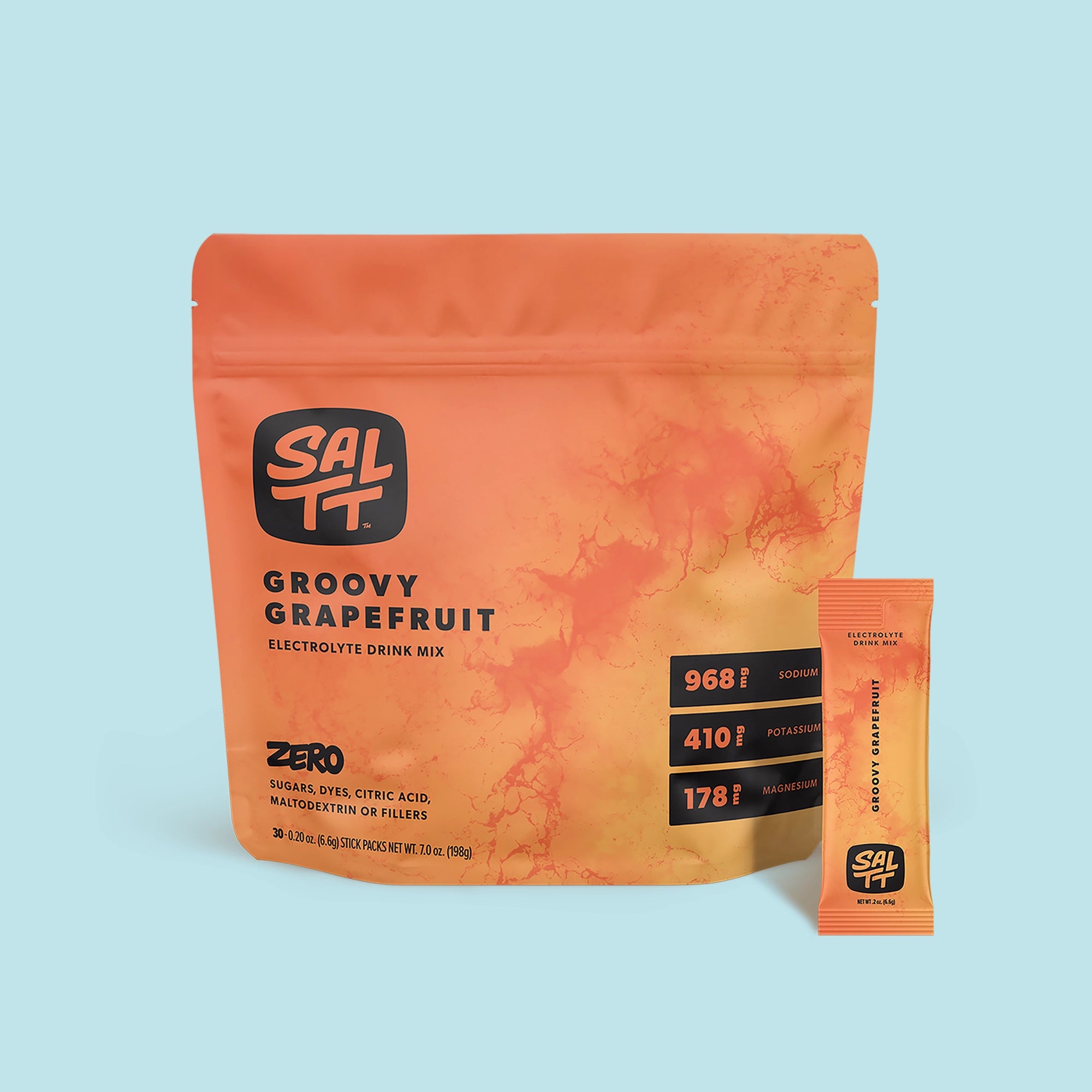 Orange SALTT Groovy Grapefruit Electrolyte Drink Mix stand-up pouch and individual stick pack. Both feature the SALTT logo and a reddish-orange ocean water splash pattern. The pouch specifies Groovy Grapefruit Electrolyte Drink Mix, ZERO SUGARS, DYES, CITRIC ACID, MALTODEXTRIN OR FILLERS, 968mg Sodium, 410mg Potassium, 178mg Magnesium, and 7.0 oz (198g) net weight. The stick pack details Groovy Grapefruit Electrolyte Drink Mix and 0.2 oz (6.6g) net weight.