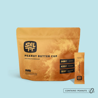 SALTT Peanut Butter Cup electrolyte drink mix pouch and single-serve stick pack in golden-brown with an ocean splash pattern.