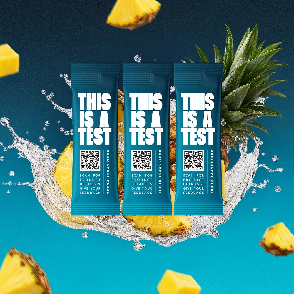 Three blue single-serve test packets labeled THIS IS A TEST surrounded by pineapple slices and water splashes on a blue background.