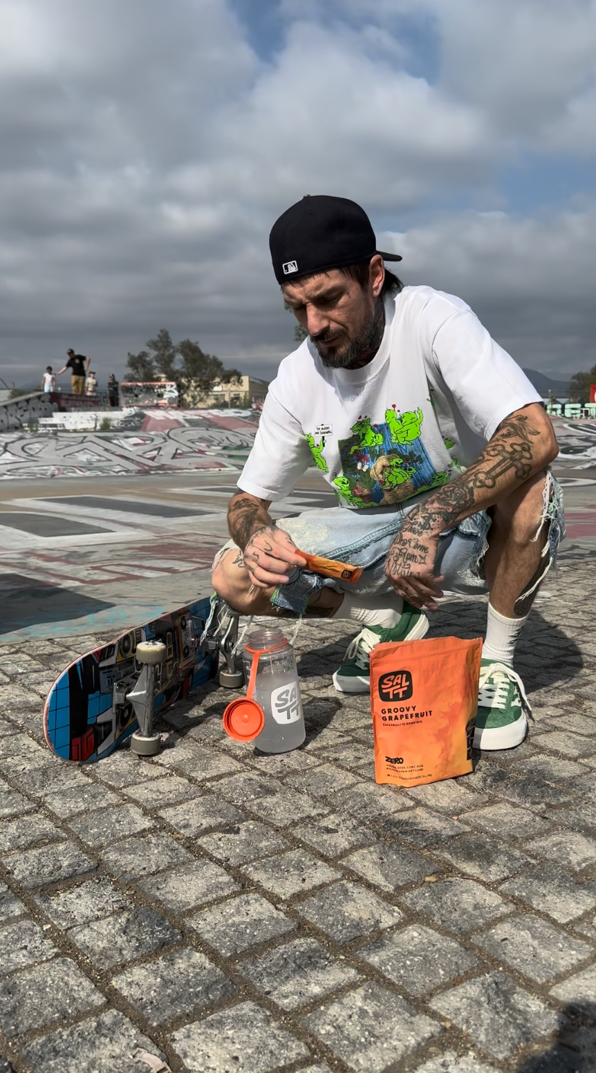 Orange SALTT Groovy Grapefruit Electrolyte Drink Mix pouch with an ocean splash pattern, zero sugars, dyes, citric acid, plus sodium, potassium, magnesium. A man holds a single-serve stick pack.
