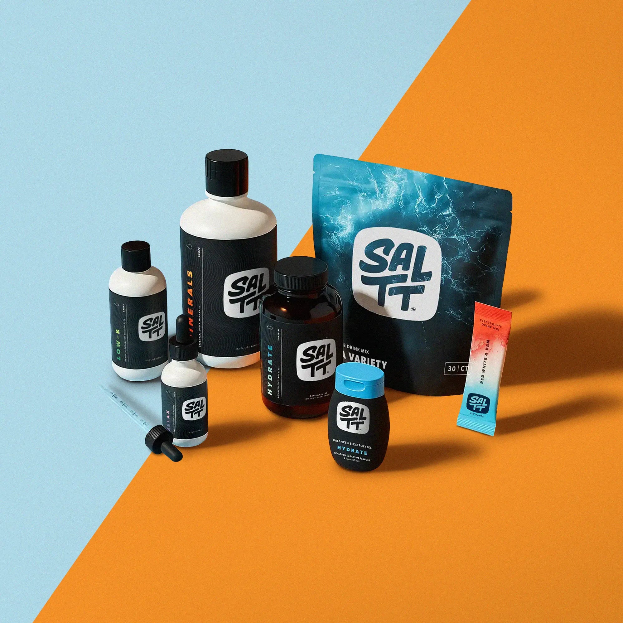 SALTT product assortment on a split blue and orange background. Features include a white Minerals bottle, a white Low-K bottle, a white Relax dropper, a brown Hydrate capsule bottle, a blue ocean splash Hydrate Drink Mix pouch, a small black Hydrate liquid bottle (zero added sugars/flavors), and a Red White & Bam electrolyte stick.