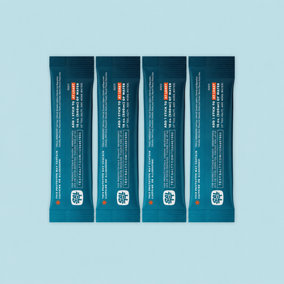 Four SALTT electrolyte drink mix single-serve stick packs. Dark teal with an ocean water splash pattern, white text, and orange warning asterisk.