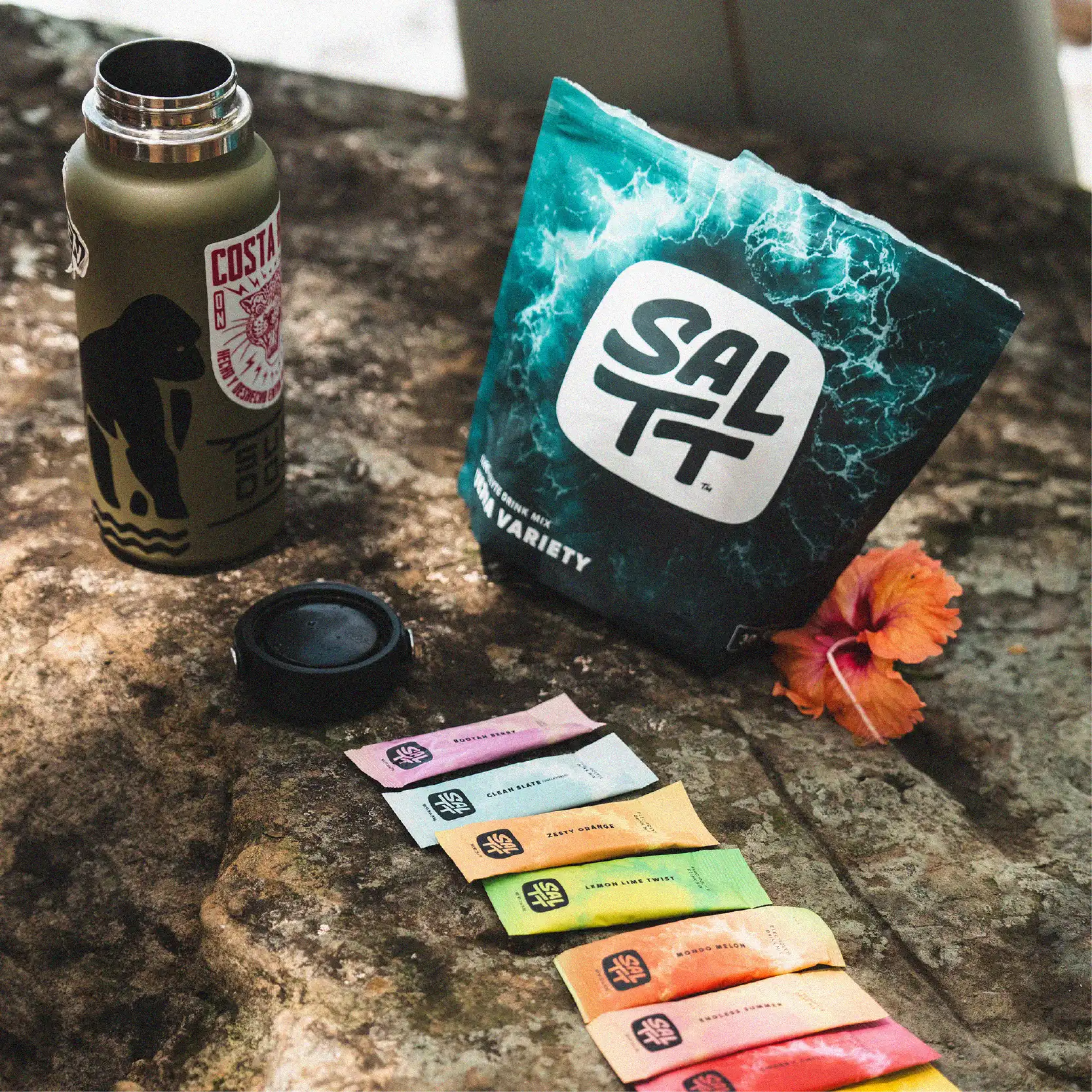 SALTT Electrolyte Drink Mix variety pouch, dark teal with an ocean water splash pattern, next to colorful single-serve stick packs.