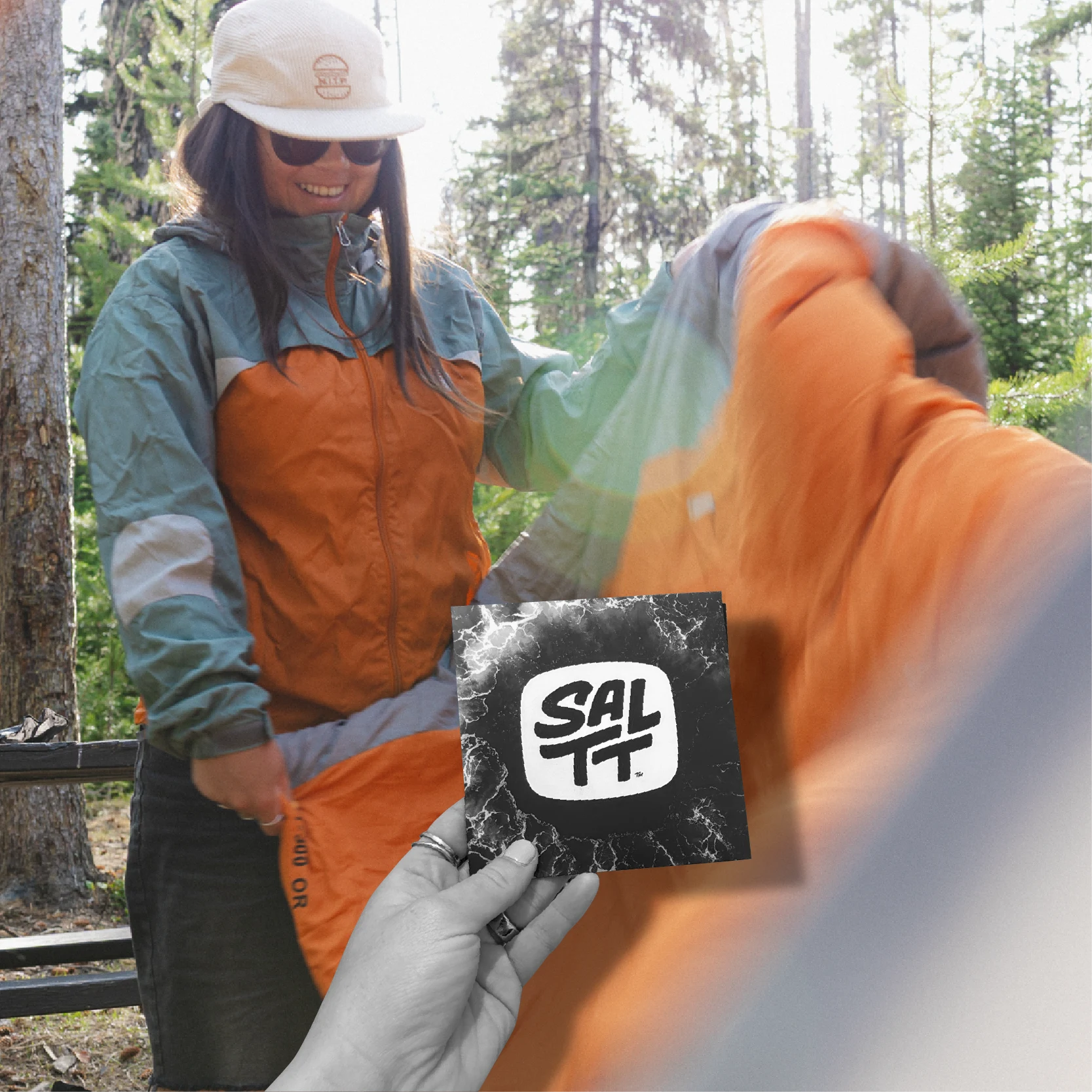 SALTT brand black and white single-serve pouch with a white ocean splash pattern, held in a hand.